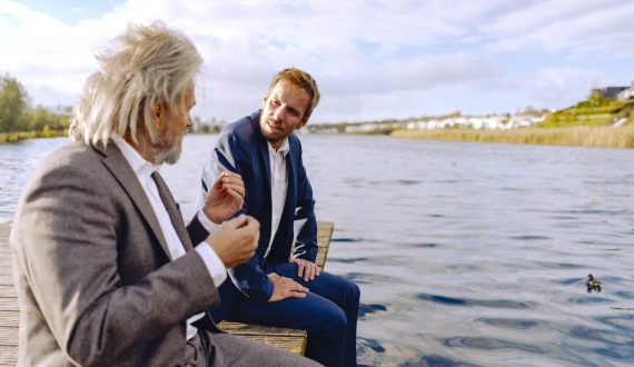 Two businessmen sitting on jetty at a lake talking