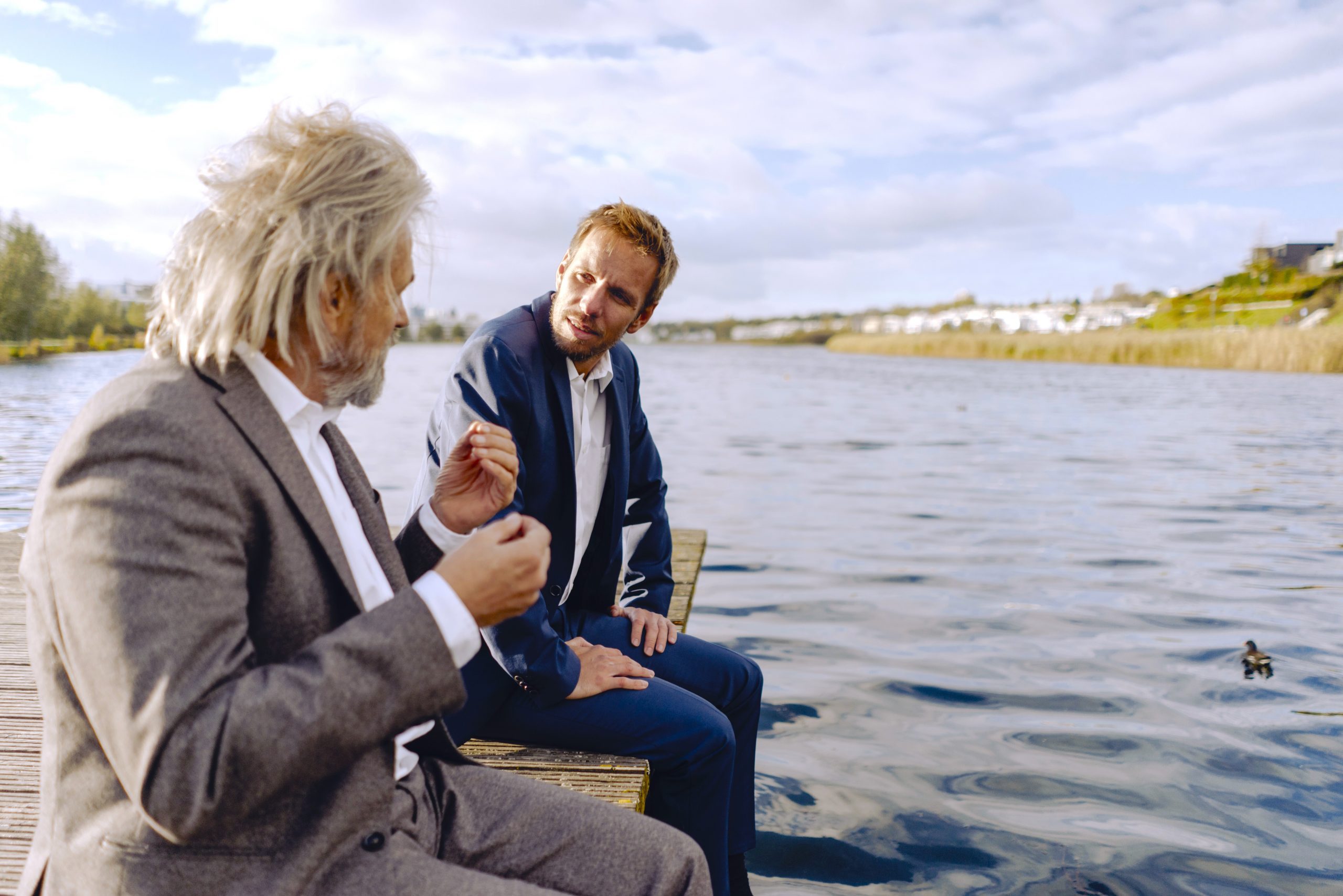 Two businessmen sitting on jetty at a lake talking